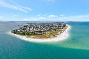 An aerial view of a coastal residential area with a beach, houses, and clear blue waters.