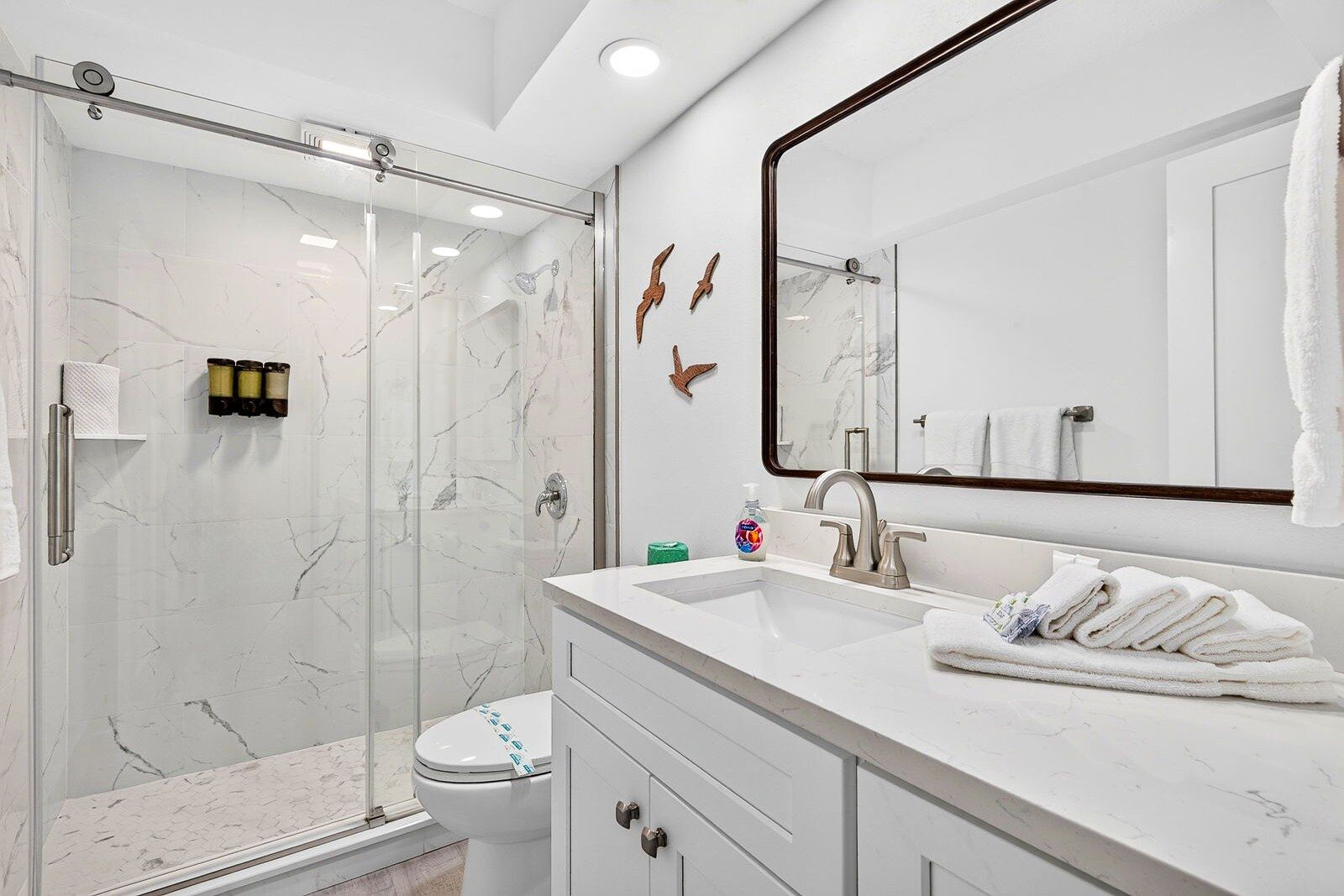 A modern bathroom with a glass shower enclosure, a white sink with a mirror, and a toilet.