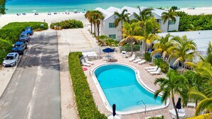 A resort with a swimming pool, beach, and parked cars.
