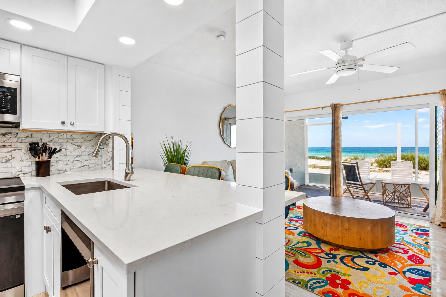 A modern kitchen with a large island, a dining area with a view of the beach, and a ceiling fan.