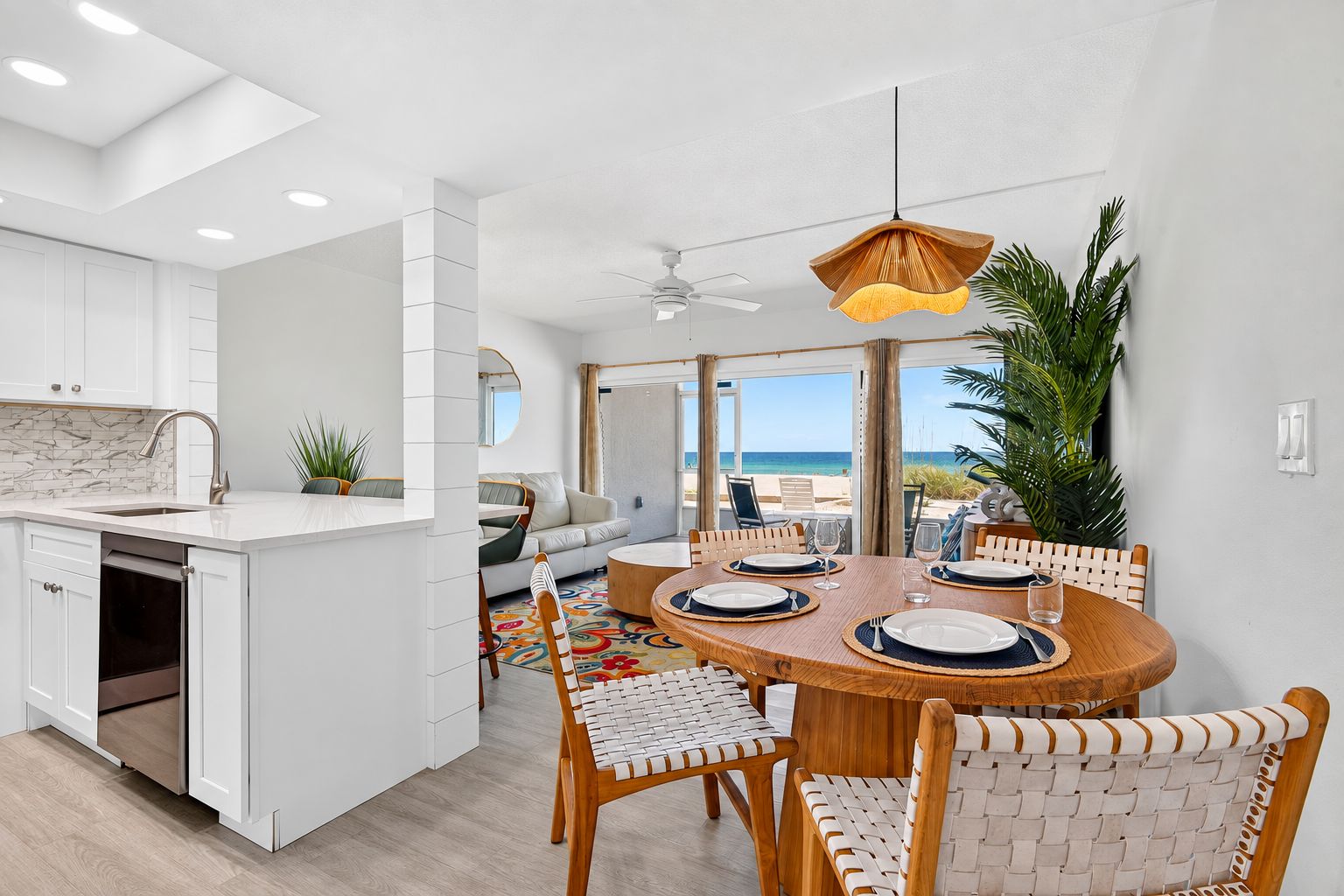 A modern kitchen with white cabinetry, a dining area with a round wooden table, and a view of the beach.