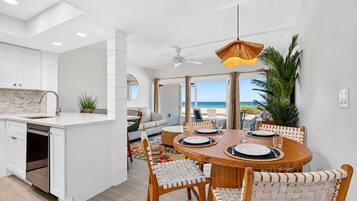 A modern kitchen with white cabinetry, a dining area with a round wooden table, and a view of the beach.