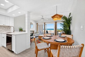 A modern kitchen with white cabinetry, a dining area with a round wooden table, and a view of the beach.