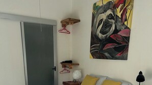 Um quarto com cama, escrivaninha, cadeira, quadro e porta.