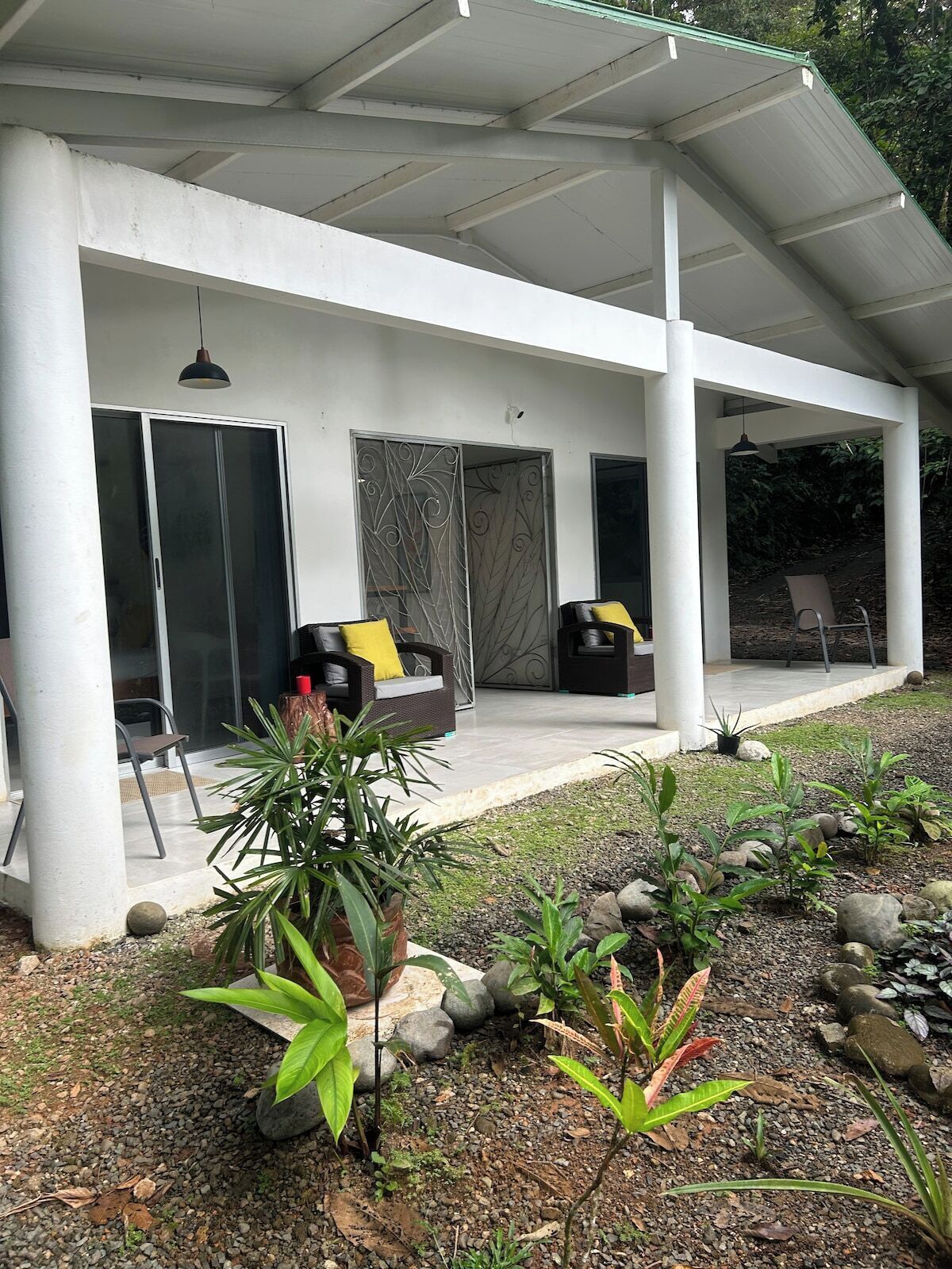 A covered outdoor seating area with a patio, a sliding glass door, and a garden with plants and rocks.