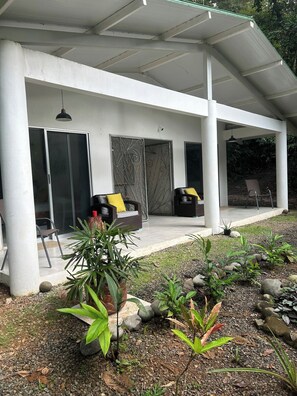 A covered outdoor seating area with a patio, a sliding glass door, and a garden with plants and rocks.