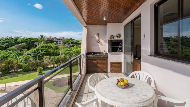Un balcón con techo de madera, una mesa de comedor con sillas y vistas a un jardín exuberante y edificios a lo lejos.