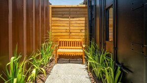 Un banco de madera en un sendero estrecho flanqueado por plantas, que conduce a una puerta de madera.