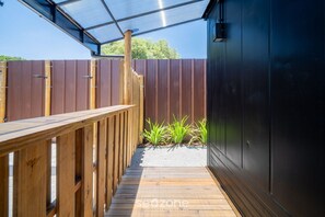 A wooden deck leading to a covered outdoor area with a metal fence and a dark building. - Chalet 200m fr/ Campeche Beach w/ Garage Scj0008 (Florianópolis)