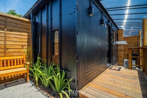 Ein modernes Gebäude mit dunkler Fassade, einer Holzterrasse und einer Sitzbank.