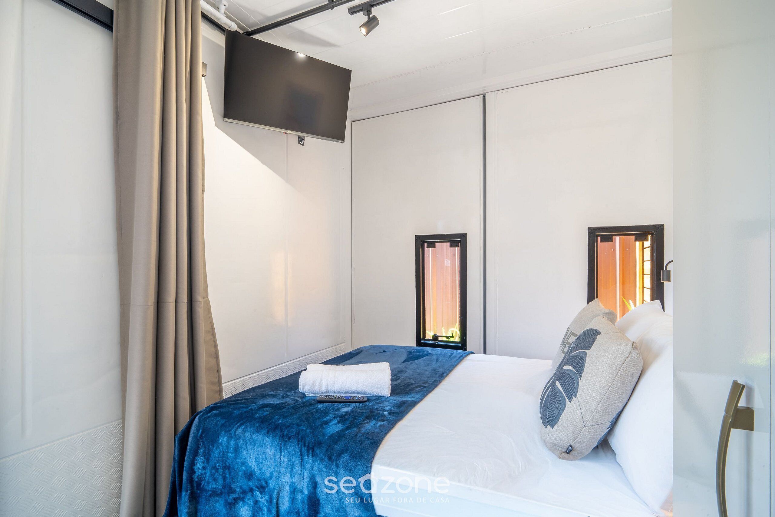 Ein modernes Hotelzimmer mit einem großen Bett, einem flachbildfernseher an der Wand und einem Fenster mit Vorhängen.
