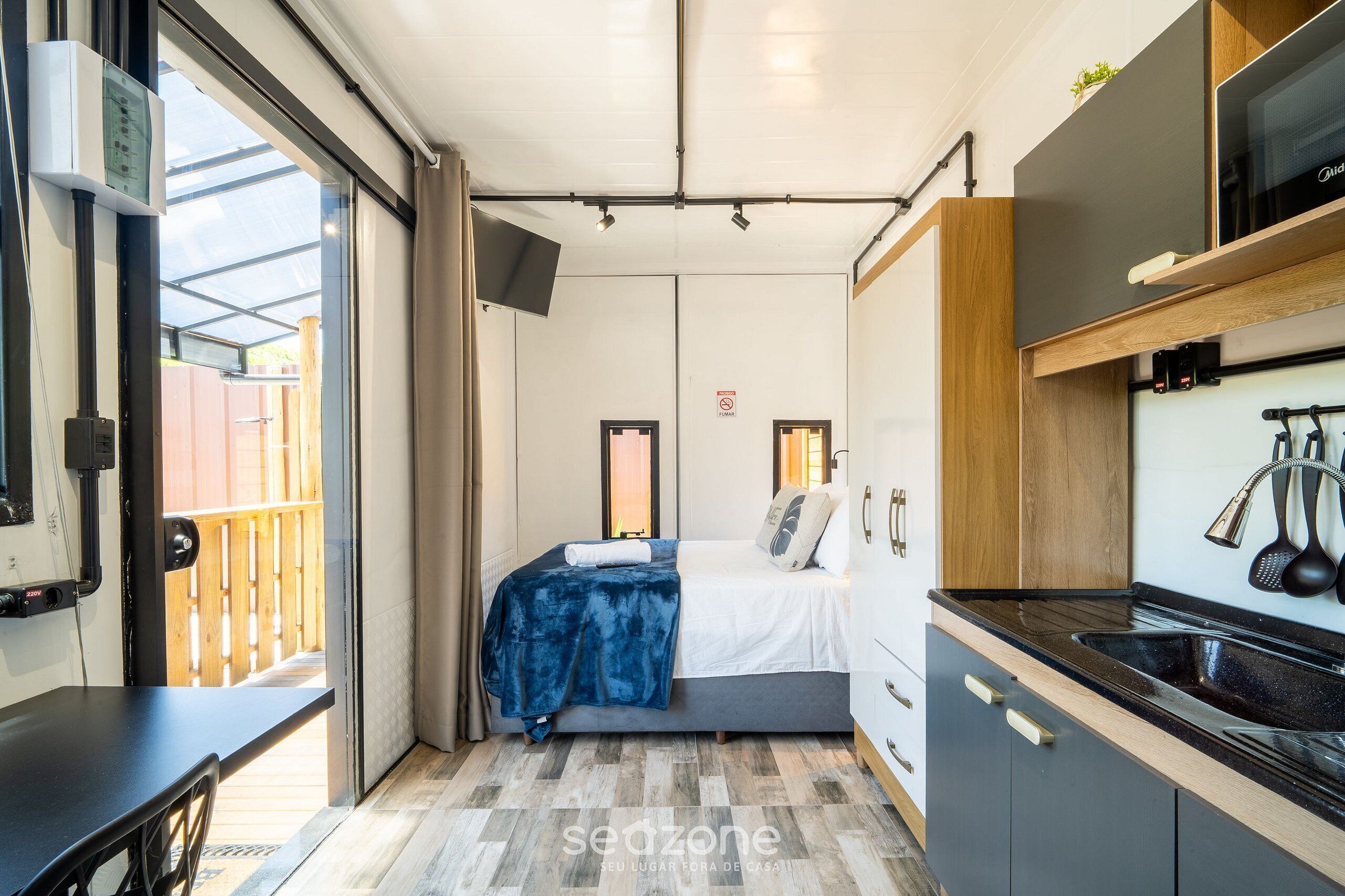A compact room with a bed, a small kitchenette, and a sliding door to an outdoor area.