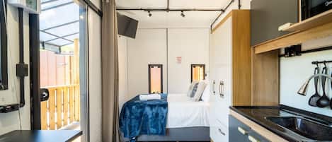A compact room with a bed, a small kitchenette, and a sliding door to an outdoor area.