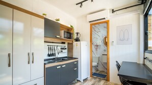 Una cocina moderna con armarios blancos, un microondas y un refrigerador. Hay una mesa de comedor con sillas y vistas al exterior a través de una puerta de vidrio.