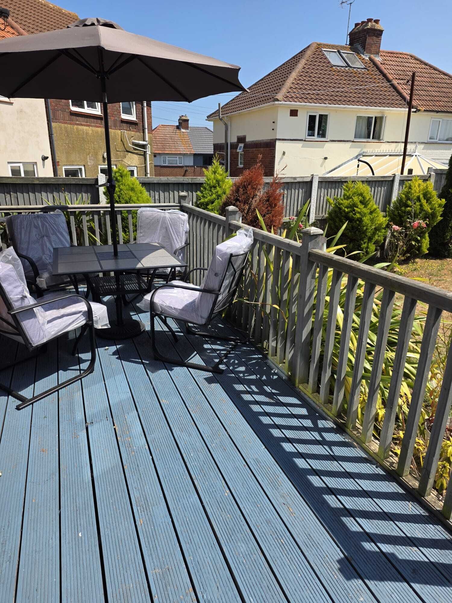 Eine Terrasse mit Tisch und Stühlen, einem schattenspendenden Sonnenschirm und einem Holzgeländer.