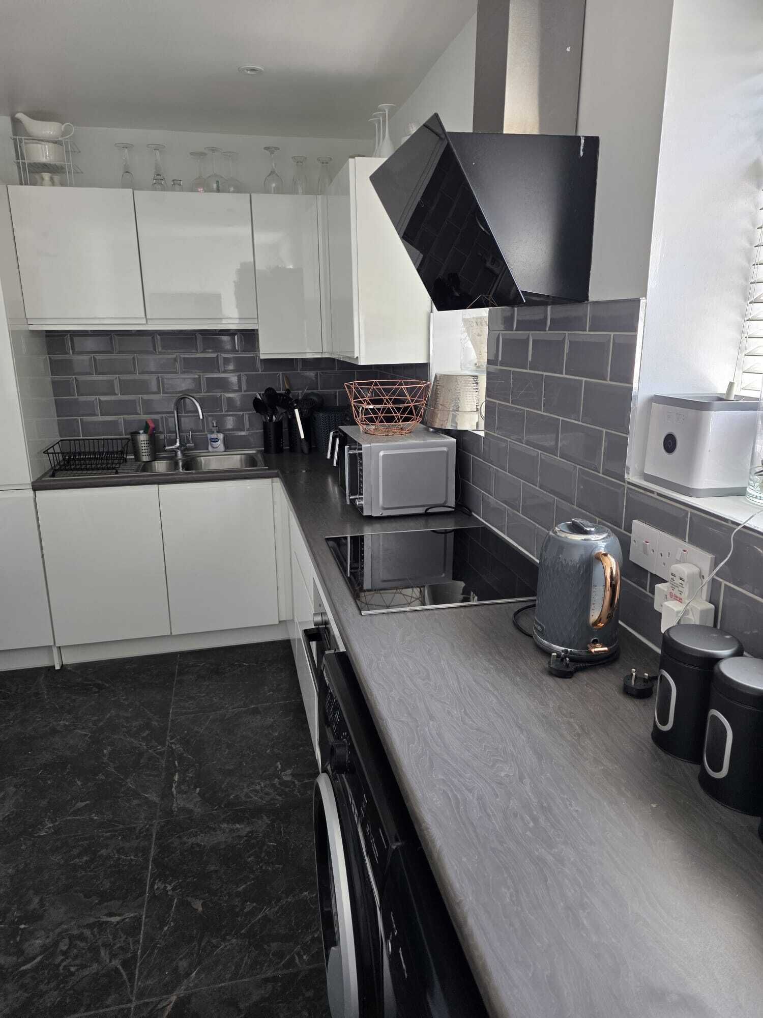 A modern kitchen with white cabinets, a black countertop, and a stainless steel sink.