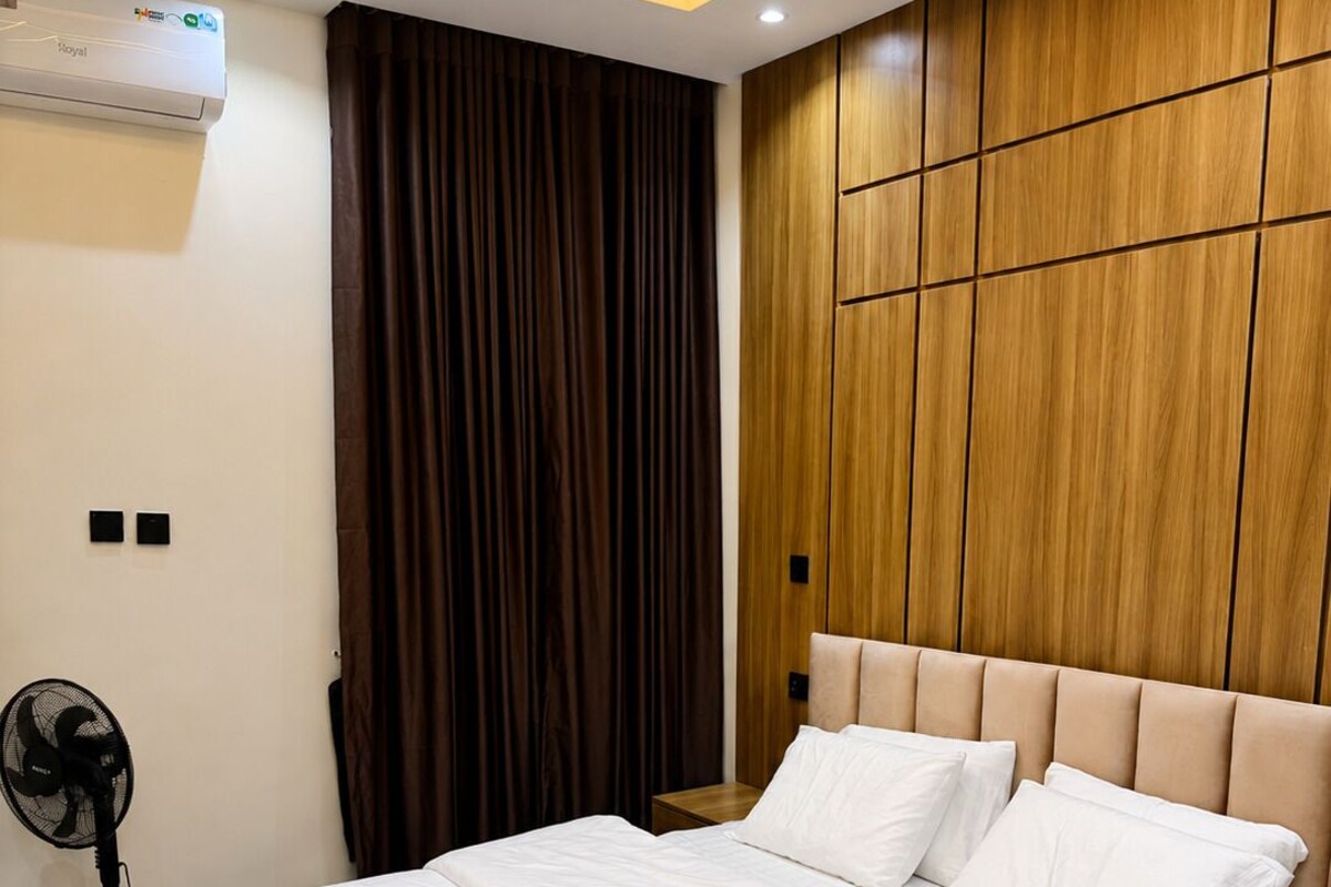 Ein Hotelzimmer mit einem Bett, einer wandmontierten Klimaanlage, einem Standventilator und einer Wandverkleidung aus Holz.