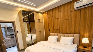 A modern bedroom with a large bed, wooden panel wall, built-in wardrobe, and an air conditioning unit. - Futuretrendhomes (Abuja)