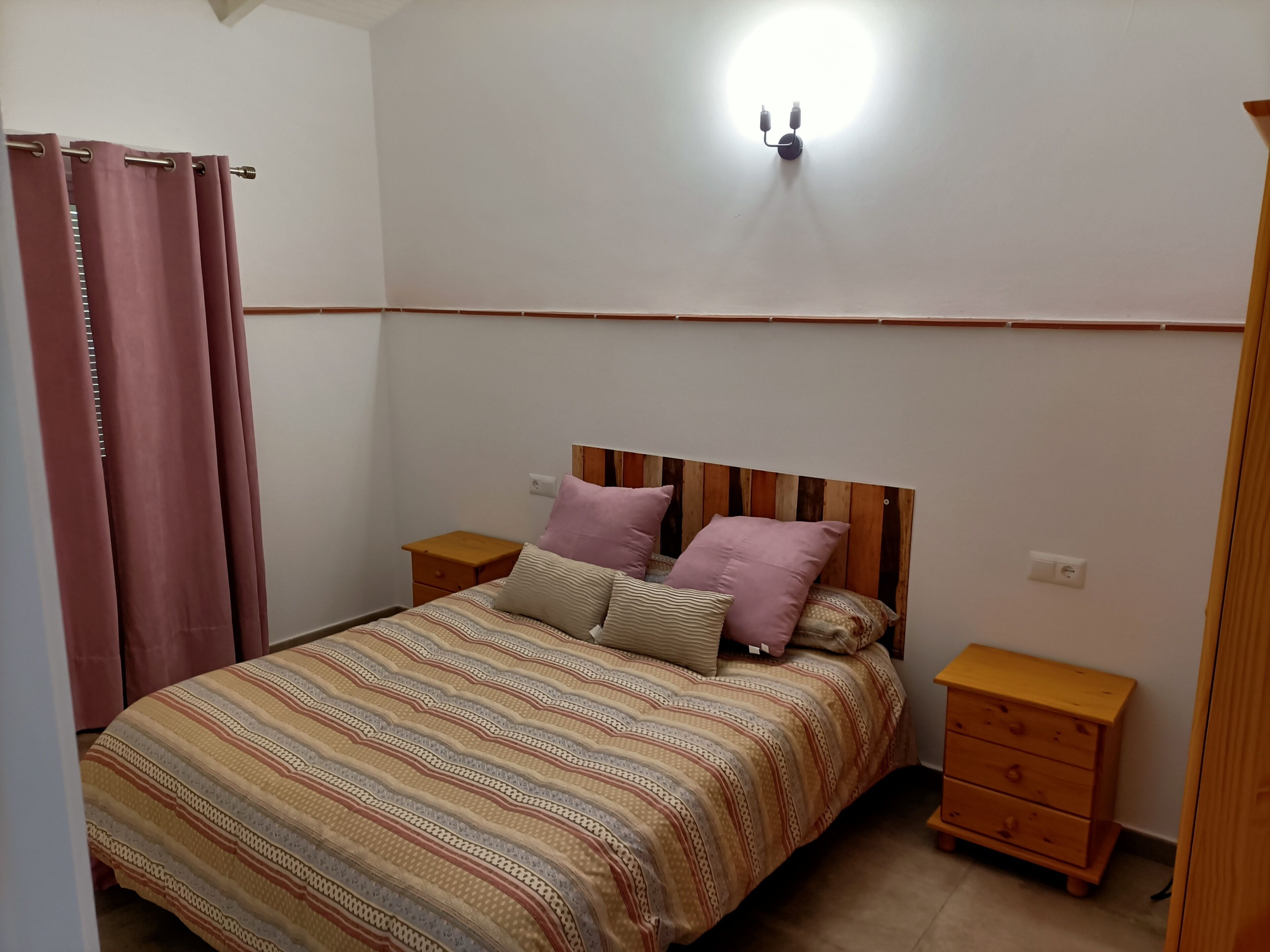 Une chambre à coucher comprenant un lit, deux tables de chevet, une tête de lit en bois, une lampe fixée au mur et une commode en bois.