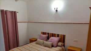 Quarto com cama, duas mesas de cabeceira, cabeceira de madeira, luminária na parede e cômoda de madeira.