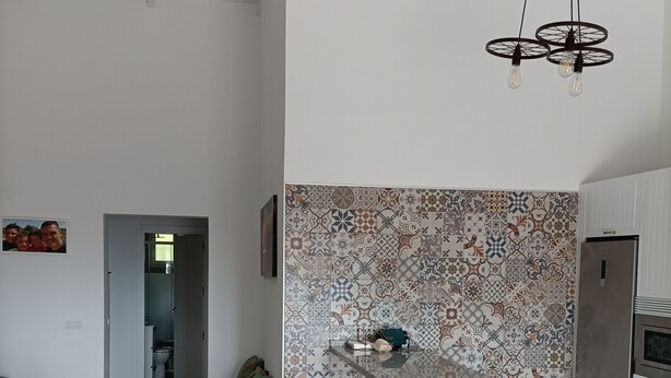 Uma cozinha moderna com painel decorativo, uma geladeira de aço inoxidável e uma área de refeições com banquetas brancas.