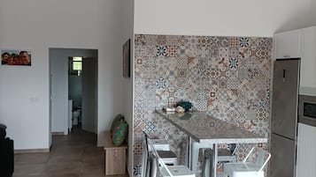 Une cuisine moderne avec un mur de crédence à motifs, un réfrigérateur en acier inoxydable et un coin repas agrémenté de tabourets blancs.