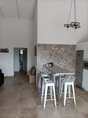 A modern kitchen with a patterned backsplash, a stainless steel refrigerator, and a dining area with white stools.