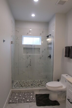 A bathroom with a glass-enclosed shower, a toilet, and a window. - Modern 2BR Houston Retreat 10 Min to Downtown (Houston)