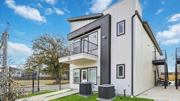 Ein modernes Wohnhaus mit zwei Etagen, einem Balkon, einem eingezäunten Garten und zwei Klimaanlagen.