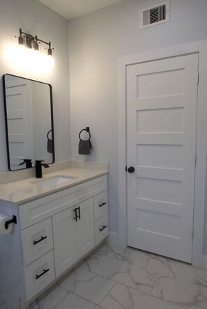A bathroom with a white sink, a mirror, a towel ring, and a door. - Modern 2BR Houston Retreat 10 Min to Downtown (Houston)
