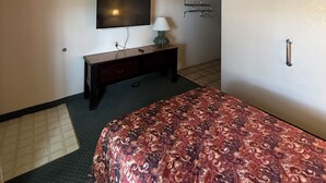 A hotel room with a bed, a TV mounted on the wall, a desk with a lamp, and a door with a handle.
