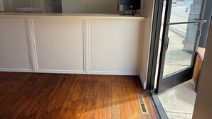 Una habitación con piso de madera, una televisión de pantalla plana sobre un soporte, una puerta y una ventana con vista al exterior.