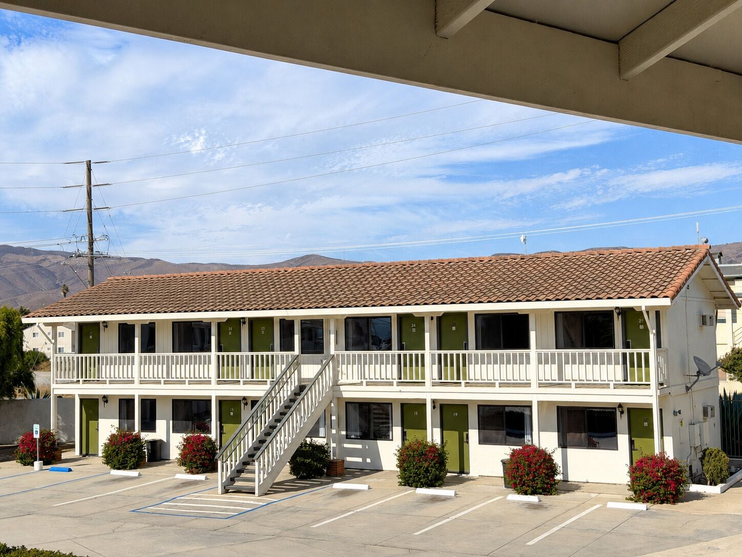 A two-story motel with a central staircase, multiple rooms with green doors, and a parking lot.