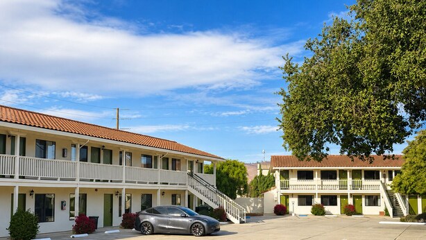 A motel with a parking lot, a car parked in the lot, and a tree in the foreground.