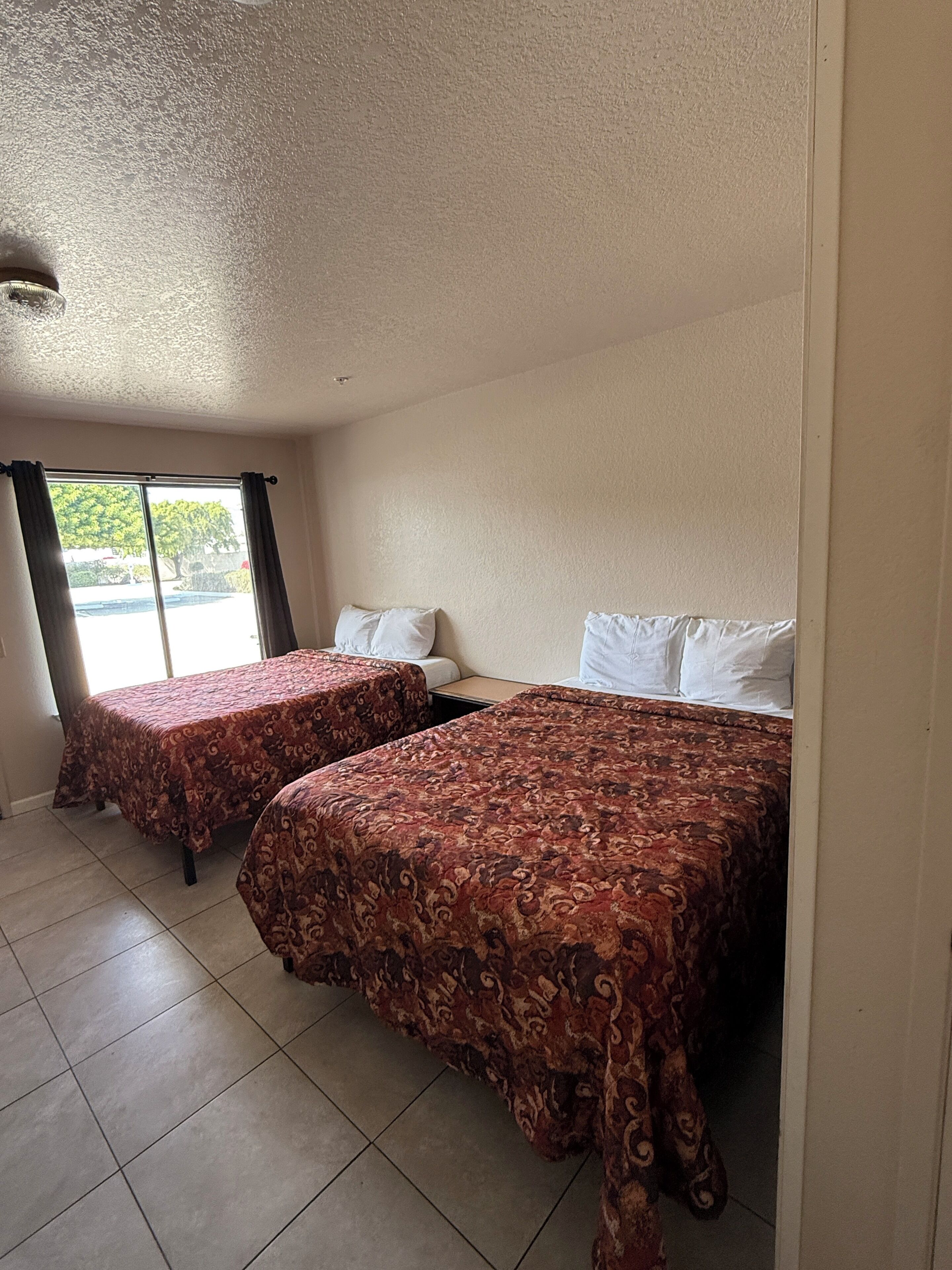 Una habitación de hotel con dos camas, una ventana con cortinas y suelo de baldosas.