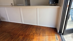 A hotel room with a wooden floor, a reception desk, a television, and a door leading to a hallway.