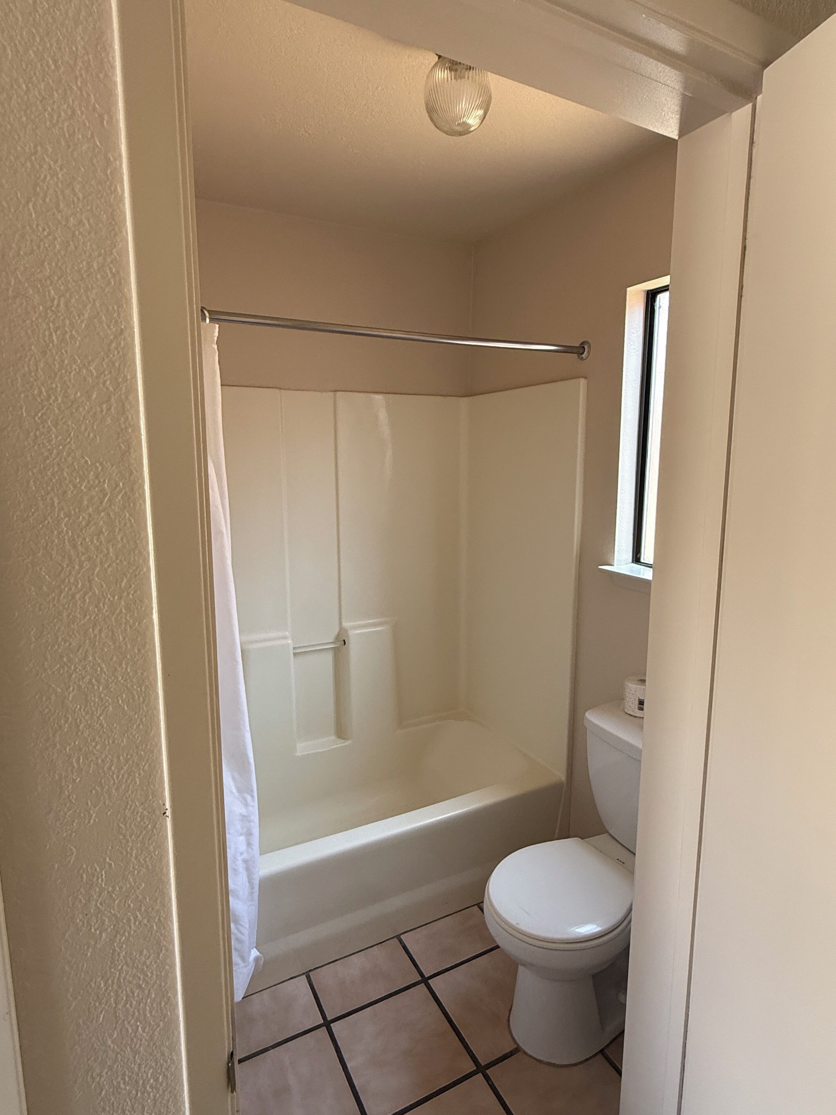A bathroom with a shower, toilet, and a window.
