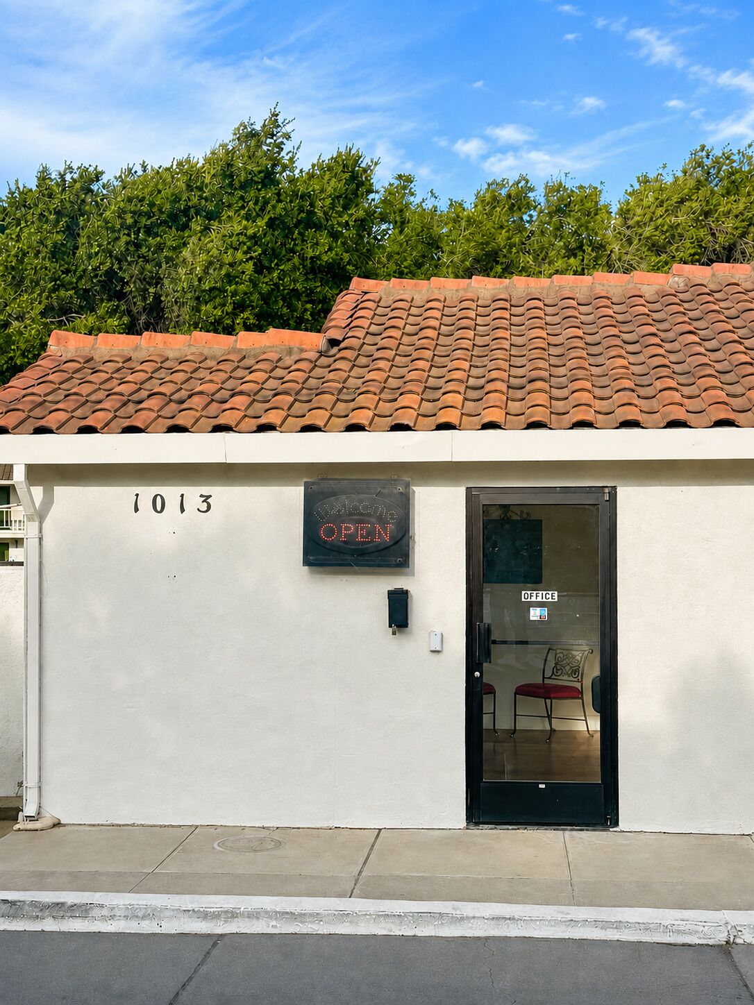 Een gebouw met een pannendak, een deur met de tekst 'OFFICE' en een bordje waarop '1013 OPEN' staat.