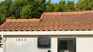 Un edificio con techo de tejas, una puerta con la leyenda 'OFFICE' y un letrero que indica '1013 ABIERTO'.