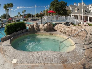 A hot tub surrounded by rock formations, with a pool and lounge chairs in the background. - Orlando | Compact Disney Retreat | Pool + Waterpark (Lake Buena Vista)