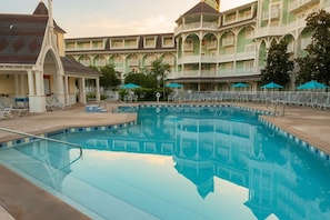 Ein Pool mit Spiegelung, umgeben von Liegestühlen und Sonnenschirmen, mit einem mehrstöckigen Gebäude im Hintergrund.