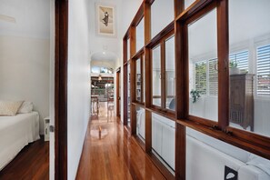 Ein Flur mit Holzboden, einem weißen Sofa und einem großen Fenster mit Jalousien.