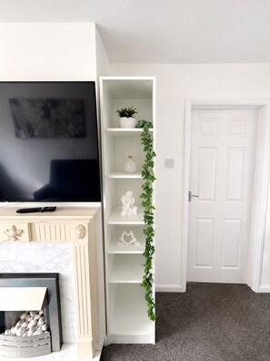 A living room with a white entertainment unit, a flat-screen TV, a fireplace, and a door. - Spacious 3BR Home | Near Huddersfield Town Centre, University & M62 (Huddersfield)