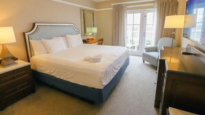 Une chambre d’hôtel avec un grand lit, un bureau, une chaise, une télévision et un balcon avec des rideaux.