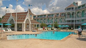 Un espace piscine aménagé avec des chaises longues et des parasols, entouré d’un bâtiment doté de nombreux balcons.
