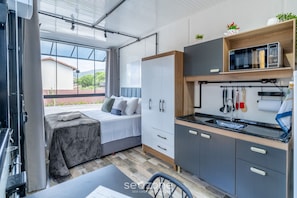 Ein kleines Zimmer mit Bett, Küchenzeile und Fenster mit Blick auf Grünflächen.