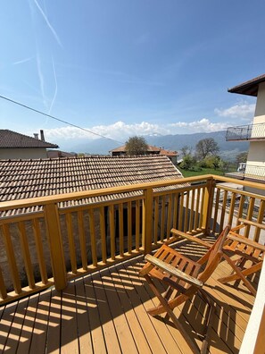 Una terraza de madera con barandilla, una silla y vistas a casas y montañas al fondo.