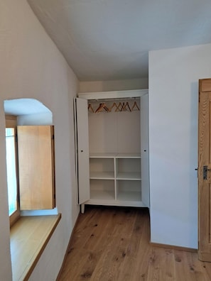 Una habitación con piso de madera, un armario blanco con espacio para colgar ropa, y una puerta de madera.