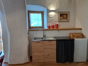 Eine kleine Küche mit Holzarbeitsplatte, Spüle, kleinem Kühlschrank und einem Fenster mit Vorhängen.
