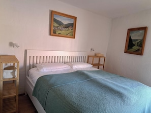 Ein Schlafzimmer mit einem Bett, einem Nachttisch aus Holz, einer Wandleuchte und zwei gerahmten Bildern.